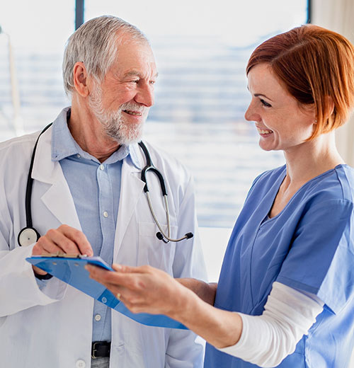 two medical professionals exchanging information on a clipboard and smiling at each other